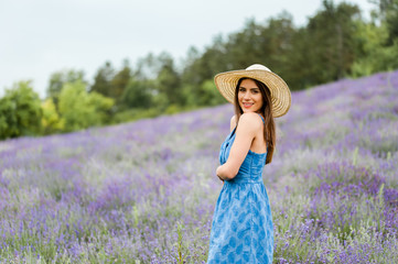 Portrait of a young beautiful woman sitting in the middle of a lavender field,  wearing a elegant blue dress and a straw hat, looking at camera.