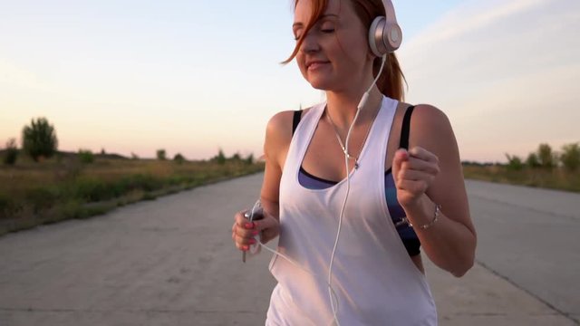 young woman runs and listens to music on headphones on a summer afternoon at sunset, close-up