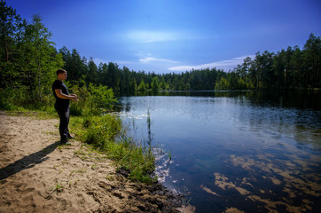 man is fishing on a forest lake
