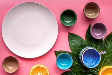 Empty plate mockup. Cups and plates near tropical leaves and fruits on pink background top view