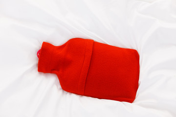 Warm red hot water bottle on white bedding