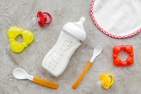 preparation of mixture baby feeding with infant formula powdered milk in bottle, spoon and toys on gray background top view