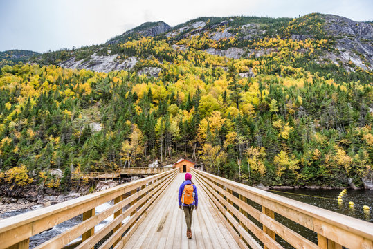 Hike Woman With Backpack Walking In Forest Nature Outdoors Bridge. Canada Travel Hiking Tourism At Hautes-Gorges-de-la-Riviere-Malbaie National Park. Active Tourist Lifestyle.