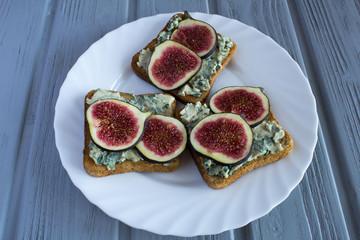 Toasts with blue cheese and figs on the white plate on the grey wooden background