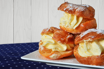 Cream puff profiterole with vanilla custard sprinkled with powdered sugar on white plate over napkin