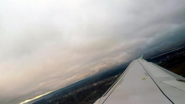 Canted angle shot over wing of airplane as it penetrates the clouds over Montreal, Canada, as the sun rises on a cloudy day.