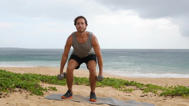 Dumbbell Squat exercise - fitness man doing squats exercising legs outdoor on beach. Fit male athlete showing exercises.