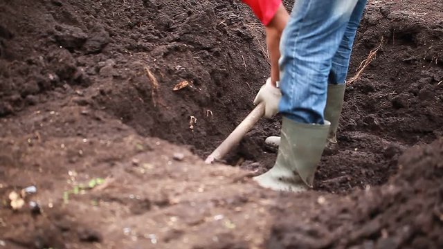 Video man in rubber boots digs a pit in the ground with a shovel
