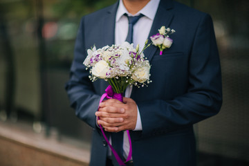 Groom in blue jacket take wedding bouquet with boutonniere with baby's breathe and rose