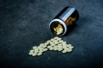 Medicines, supplements in a glass bottle. Pills spilling out from glass bottle. Medicine´s background. Pharmacy. Close up of capsules. Pack of tablets on a black background.