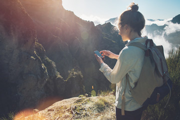 Pretty traveling woman standing on top of  mountain at sunset and using mobile phone.