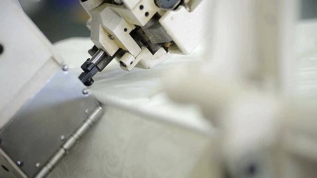 Hands on a vertical machine makes a side seam on a mattress factory. Factory worker controls the sewing machine and threads the angle on the frame.