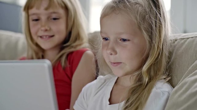 Medium shot of laughing little girls with blond hair laughing and taking pictures on tablet