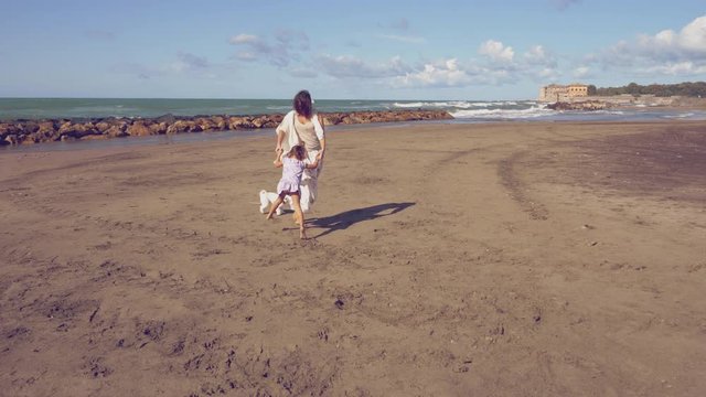 Beautiful woman with little daughter and dog dancing and jumping happy on beach  4K slow motion retro style