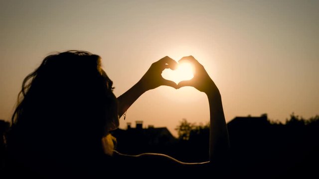View of adorable woman silhouette holding sun in the field with a warm and vague background In summertime