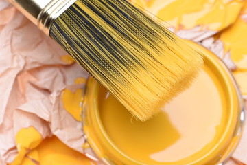 Paintbrush and can lid  with yellow paint, closeup