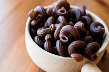 Raw Brown Pasta with Grape seeds in wooden ladle.
