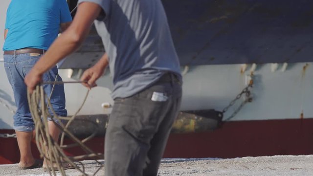 Two Male Harbour Workers Collecting Rope Of A Ferry Boat In Greece