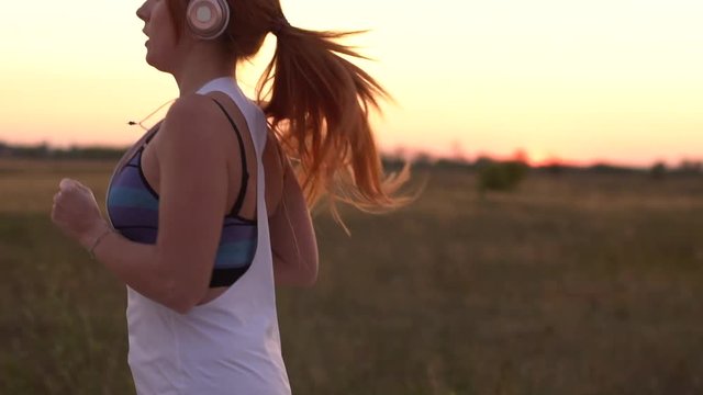 young woman runs and listens to music on headphones on a summer afternoon at sunset, close-up, slow motion