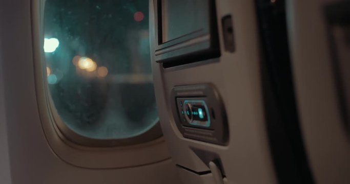 Airplane cabin. View to the seat-back monitor with control pad and night lights of airport in the illuminator