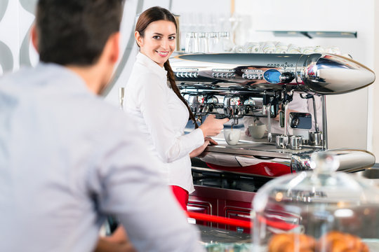Attractive waitress smiling to male customer while preparing espresso at the automatic coffee machine indoors - Powered by Adobe