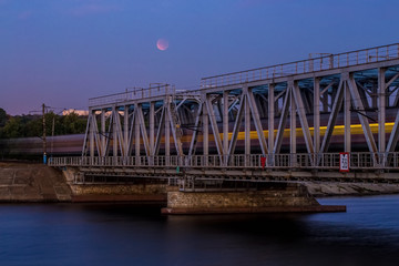 Train is passing through railway bridge, long exposure. Moon eclipse on the sky 