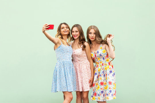 Three beautiful sisters in dress, macking selfie on green background,