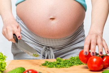 Female hands cut salad in the kitchen, woman is pregnant, the stomach is close-up