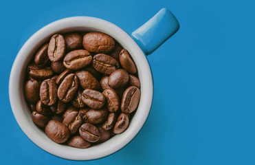 Blue small espresso cup with coffee seeds inside isolated on blue.