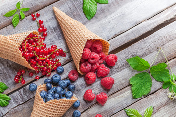 Blueberries, red currant and raspberries in ice cream cones with green leaves on old white rustic wooden table in studio