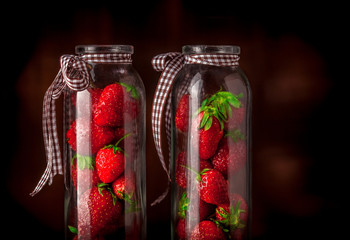 Strawberries closeup in studio in two glass jars on dark background