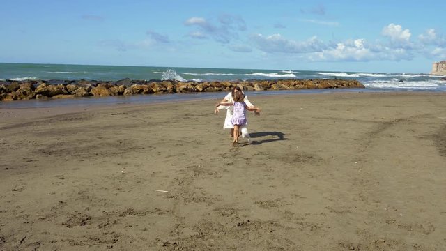 Little girl running towards mother on beach 4K slow motion
