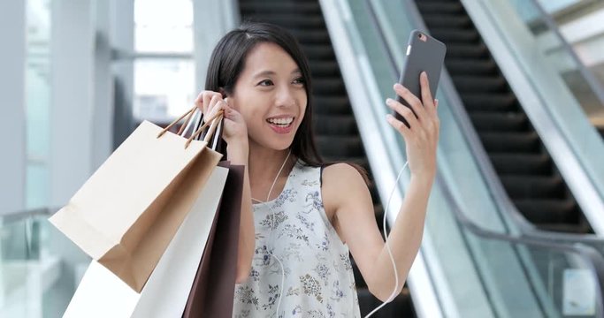 Woman talking on cellphone with video call and holding shopping bags