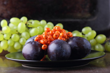 Green grapes, blue plums and orange rowan berries on a black plate for designer in retro style