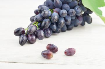 Three scattered grapes beside bunch of fresh ripe blue grapes with green leaf on old wooden rustic white planks