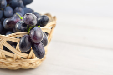 Full wicker basket of fresh ripe blue grapes on old wooden rustic white planks