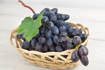 Bunch of fresh ripe blue grapes with green leaf in wicker basket on old wooden rustic white planks