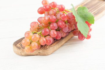 Fresh ripe pink grapes with green leaf on brown cutting board on old wooden rustic white planks