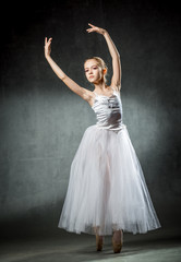 Fototapeta premium Beautiful young ballerina is dancing in the studio on a dark background. A little dancer. Ballet dancer.
