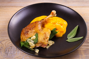 Roast duck leg with mashed pumpkin (butternut squash), sage and garlic on plate, closeup, horizontal