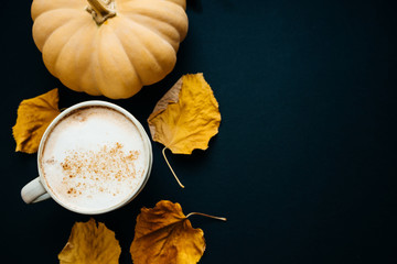 Pumpkin spiced latte or coffee in cup, dry leaves, gifts on black table. Autumn or winter hot drink. Space for text