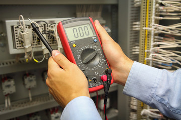 Multimeter in hands of electric engineer on background of automation control panel.
