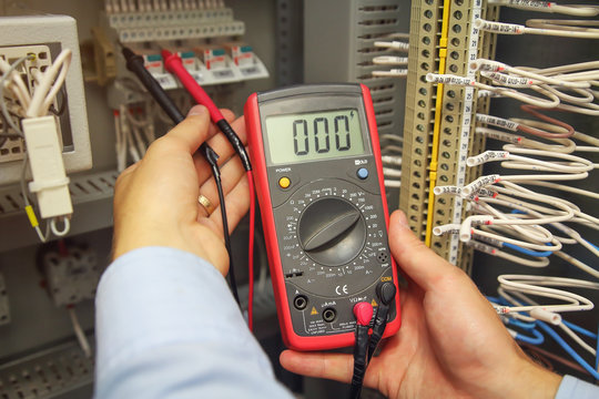 engineer tests industrial electrical circuits with multimeter in control terminal box. Engineer's hands with multimeter close-up against background of terminal rows of automation panel