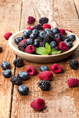 Ripe and sweet berries in bowl on wooden background