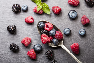 Ripe and sweet berries in vintage metal spoon on black background