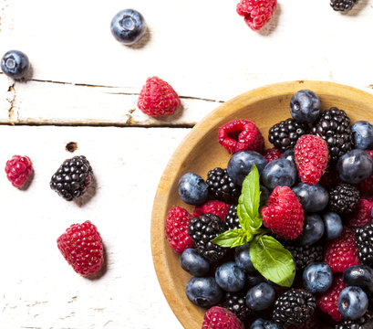 Ripe and sweet berries in bowl on wooden white background