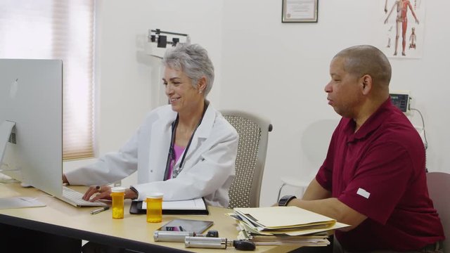 Doctor talking to male patient and checking computer