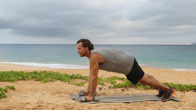 Dumbbell Plank Row. Fitness man doing Alternating Renegade Row exercise using dumbbells while exercising outside on beach. SLOW MOTION video.
