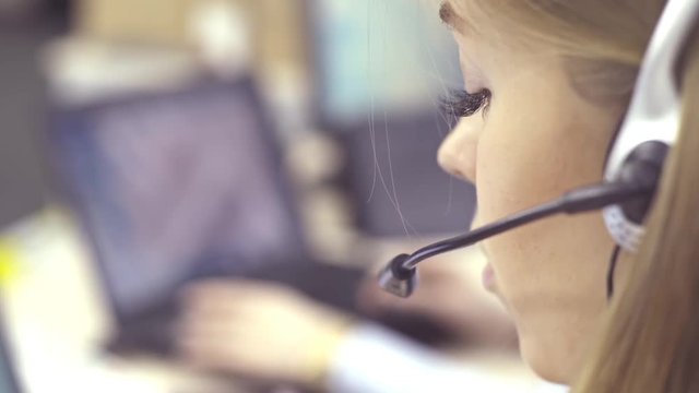 The operator of the hotline with headsets, sit at the computer in the office and advise clients. Workers call-center, a woman talking to customers. She prints on the computer and answers questions.