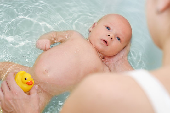 Caucasian woman is holding her newborn baby on the water while he bathing
